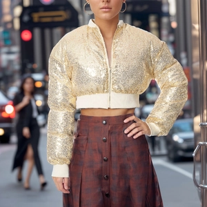 Close-up of golden sequin cropped bomber jacket with cream ribbed cuffs and metal zipper