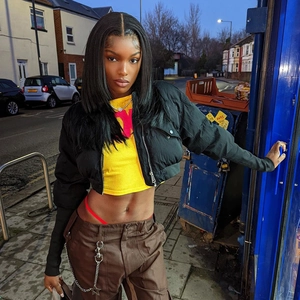 Detail of a shiny black puffer jacket with a yellow crop top and brown cargo pants