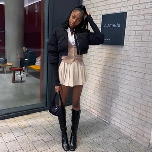 Outdoor street style view of a black slim-fit hooded jacket styled with a beige pleated skirt