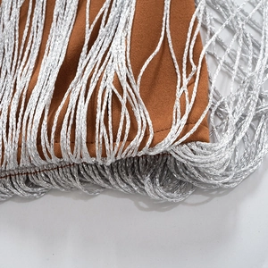 Detalle de flecos plateados y costuras en tela marrón de los pantalones de talle alto