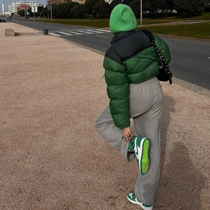 Detail of green puffer jacket styled with matching beanie and sneakers in urban street setting