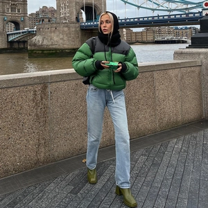 Green color-block puffer jacket styled with denim jeans and boots in a city setting