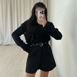Détail d'un pull en maille noire à manches longues et d'un short à taille haute ceinturé