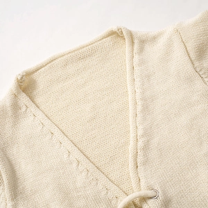 Détail de haut en maille crème col V avec bordure torsadée et lacets à œillets