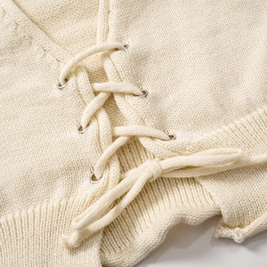 Détail d'un pull en maille crème montrant le laçage et les œillets métalliques