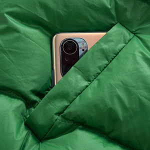 Detail view of a green puffer jacket showing a large side pocket with a smartphone inside