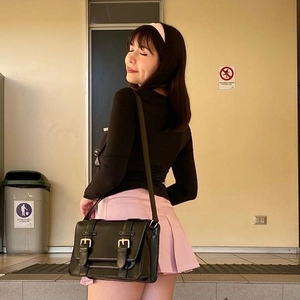 Détail d'un sac besace noir vintage à boucles porté avec une jupe plissée rose tendance