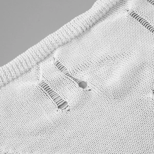 Close-up of white knitted fabric texture featuring distressed hollow out details and fibers