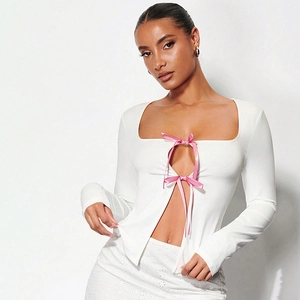 Détail d'un haut blanc à manches longues avec décolleté carré et nœuds roses satinés