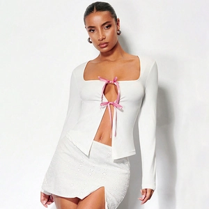 Détail de nœuds en satin rose et décolleté carré sur un cardigan blanc en tricot