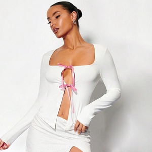 Détail du haut blanc à manches longues avec nœuds en satin rose et découpe trapèze