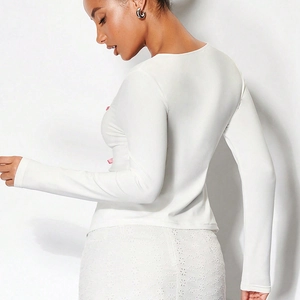 Détail d'un haut blanc à manches longues avec nœud en soie rose et jupe en dentelle