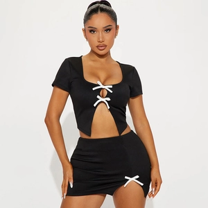 Detail van zwarte gebreide crop top met witte strikken en bijpassende mini-rok