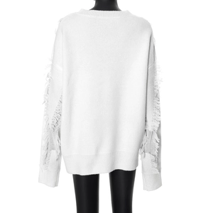 Detail view of white distressed knit sweater featuring fringe tassels on long sleeves