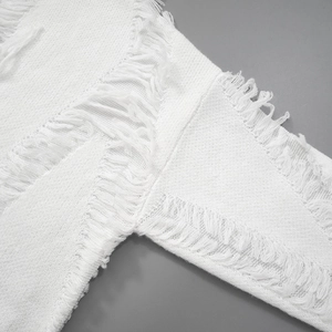 Detail of white distressed knit top featuring ripped texture and frayed fringe edges