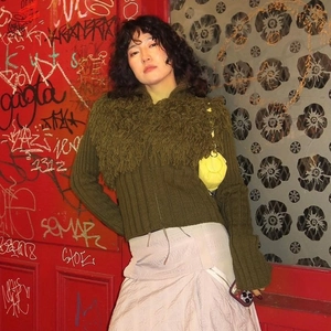 Detail of dark green knit cardigan featuring long fringe texture and ribbed fabric