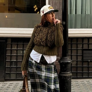 Outdoor shot of green tassel knit sweater with plaid skirt and embroidered baseball cap
