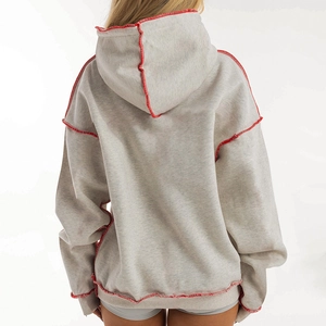 Macro detail of the oversized grey hoodie showing red raw edge stitching and seam design