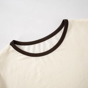 Detailaufnahme aus Strickbaumwolle mit braunem Kontrastsaum am cremefarbenen Oberteil