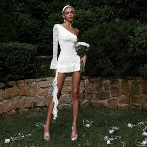 Detail of white lace one-shoulder mini dress with ruffled trail and bell sleeve in a garden