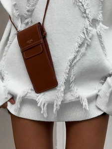 Brown leather crossbody phone bag with gold lettering over a white knit sweater