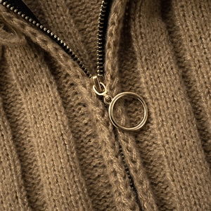 Detail shot of heavy-knit fabric with golden circular zipper ring on brown cardigan