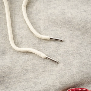 Detail of light gray hoodie fabric with cream woven drawstring and silver metal aglets