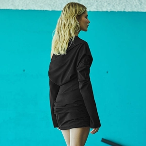 Side view of sleek black long sleeve mini dress against a bright blue studio wall