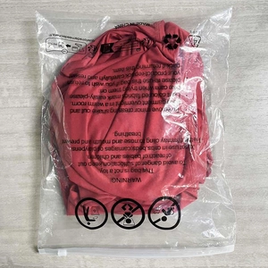 Robe courte asymétrique rouge pliée dans son emballage plastique avec avertissements