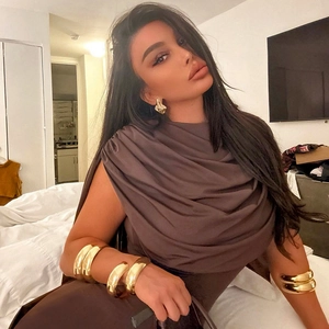 Close-up of chunky gold-toned polished bangles and wave earrings on model's wrist