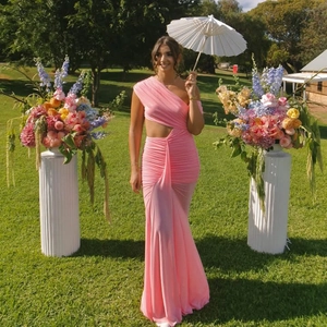 Pink one-shoulder maxi dress with waist cutout and pleated texture in a garden setting