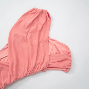 Detailed view of coral pink knit dress featuring elegant pleats and soft draped fabric