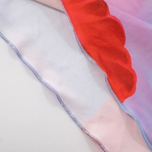 Detailed macro view of red wavy lettuce edge hem on floral print dress with blue stitching