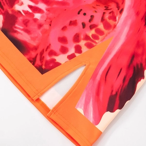 Detail of vibrant floral print dress featuring orange piping and V-split hem design