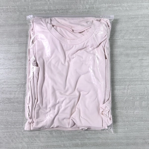 Pale pink crew neck t-shirt in transparent plastic zipper bag on grey wood background