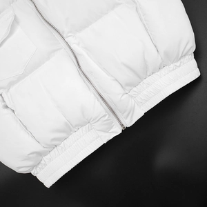 Detail of white puffer vest showing metal zipper, horizontal quilting and elastic hemline