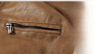 Macro detail of brown textured leather jacket featuring a silver metal zipper pocket