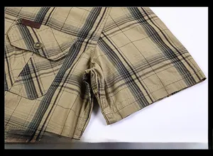 Dettaglio di una camicia a quadri kaki con tasca a bottone ed etichetta del marchio