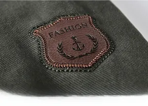 Dettaglio di una toppa in pelle marrone con logo ancora su una giacca verde a coste