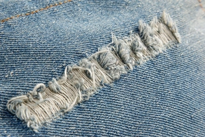 Dettaglio del tessuto denim blu con trama invecchiata e cuciture stile vintage