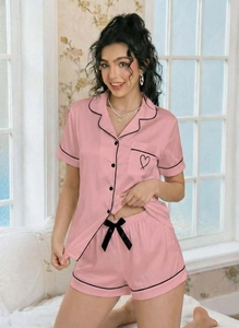Close-up of pink satin pajama set with black piping and heart detail on pocket