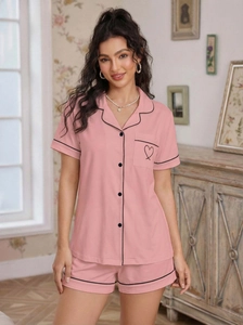 Detail of pink pajama set featuring black contrast piping and heart embroidery on pocket