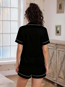 Rear view of black satin pajama set featuring white piping on short sleeves and shorts