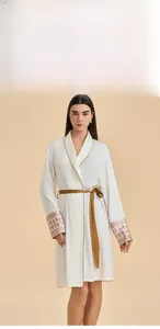 Detail of white satin robe featuring golden piping and floral embroidery on the sleeve cuff