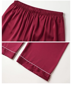 Detail of wine red satin pajama pants featuring elastic waist and white piping hem