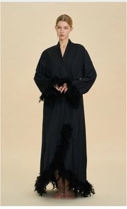 Detail of luxury long black satin robe with elegant feather trim on cuffs and hemline