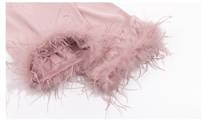 Close-up of pink satin pajama sleeve with luxurious ostrich feather cuffs and soft silk texture