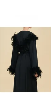 Détail d'un peignoir en satin noir avec des finitions luxueuses en plumes aux manches et au dos