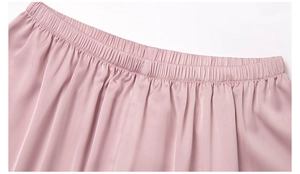 Detail view of the elastic waistband on pink satin pajama shorts with pleated texture