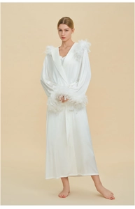Détail du peignoir de luxe blanc montrant la texture satinée et les plumes aux poignets